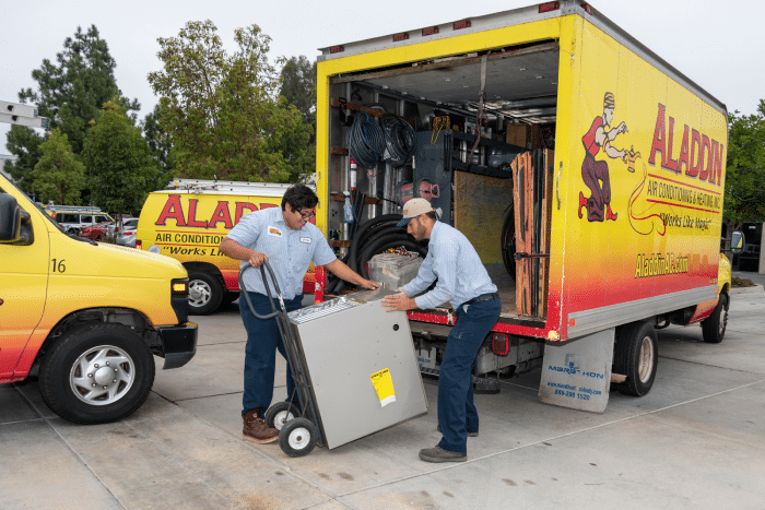 Two HVAC technicians unloading a home heating & cooling unit from an Aladdin air conditioning & heating work truck